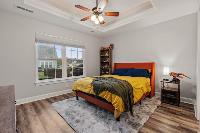 bedroom with ceiling fan, a tray ceiling, dark hardwood / wood-style floors, and crown molding