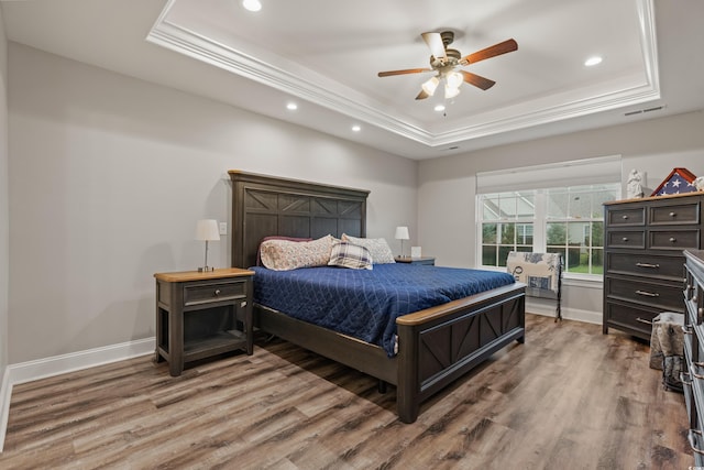 bedroom with ceiling fan, a tray ceiling, and wood-type flooring