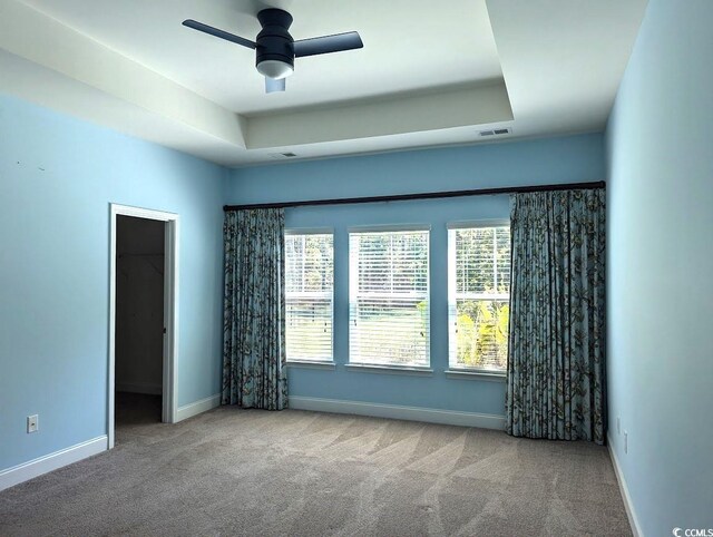 spare room with ceiling fan, light colored carpet, and a raised ceiling