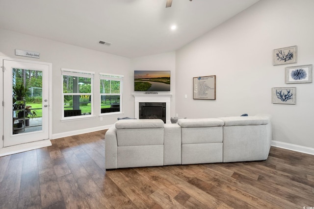 living area featuring dark wood finished floors, visible vents, a ceiling fan, a glass covered fireplace, and vaulted ceiling