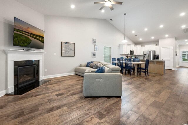 living room with dark hardwood / wood-style floors, ceiling fan, a premium fireplace, and high vaulted ceiling