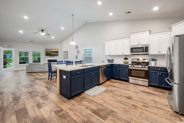 kitchen with blue cabinets, a sink, white cabinets, open floor plan, and appliances with stainless steel finishes