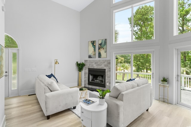 living room featuring light wood-type flooring, a tile fireplace, and a high ceiling