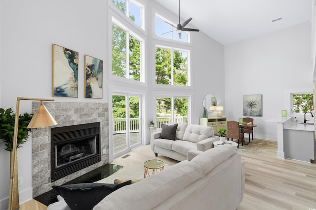 living room featuring a tiled fireplace, a high ceiling, visible vents, and light wood-type flooring