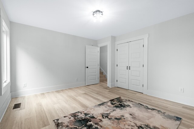 unfurnished bedroom featuring light hardwood / wood-style flooring, a closet, and multiple windows