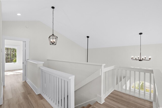 stairway with wood-type flooring, lofted ceiling, and an inviting chandelier