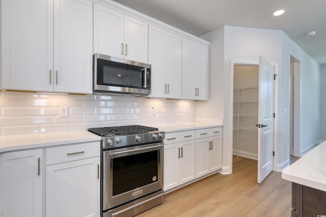 kitchen with white cabinetry, stainless steel appliances, light hardwood / wood-style floors, and backsplash