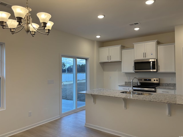 kitchen featuring white cabinetry, light stone counters, pendant lighting, a kitchen bar, and appliances with stainless steel finishes