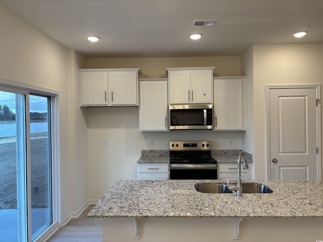 kitchen featuring white cabinets, stainless steel appliances, light stone counters, and sink