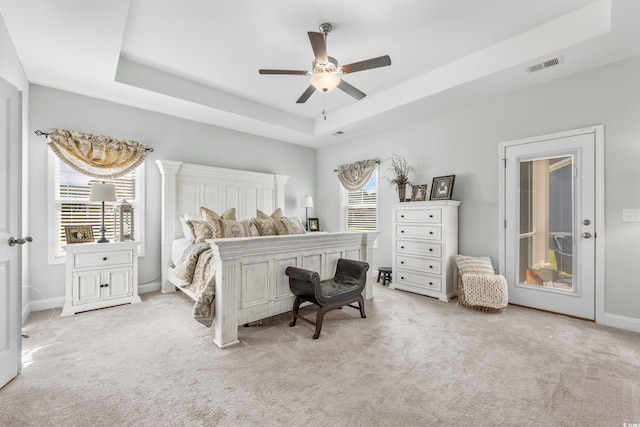 bedroom featuring ceiling fan, multiple windows, and a tray ceiling