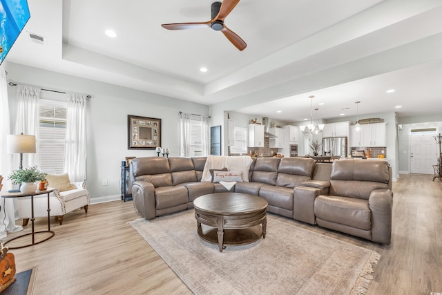 living room featuring ceiling fan with notable chandelier, light hardwood / wood-style floors, and a tray ceiling