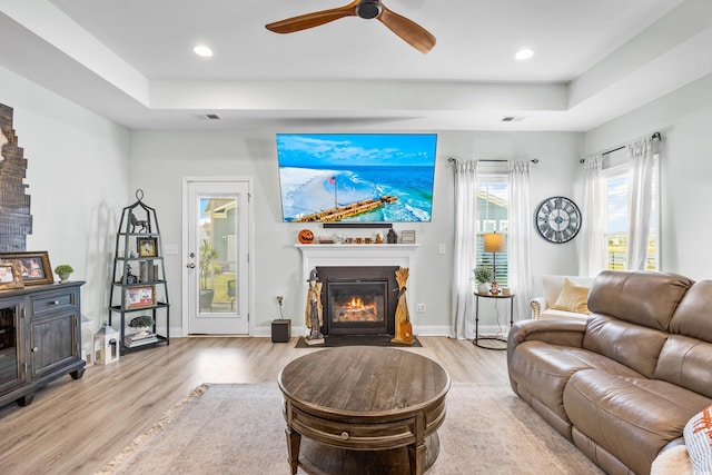 living room with light wood-type flooring, ceiling fan, and a raised ceiling