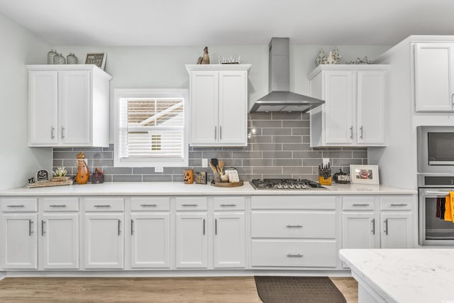 kitchen featuring stainless steel appliances, wall chimney range hood, white cabinetry, and decorative backsplash