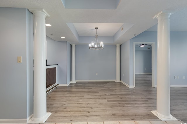 unfurnished dining area featuring light hardwood / wood-style flooring, a textured ceiling, a tray ceiling, and ceiling fan with notable chandelier