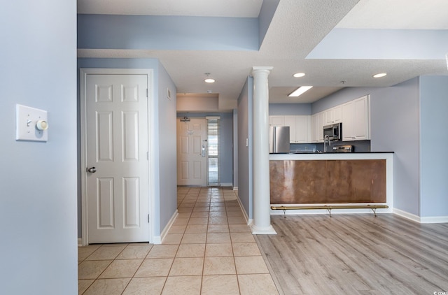 kitchen with ornate columns, light hardwood / wood-style flooring, stainless steel appliances, white cabinetry, and a textured ceiling