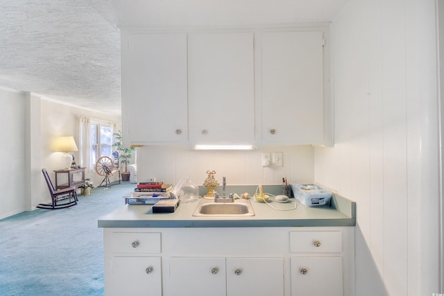 kitchen with a textured ceiling, sink, carpet flooring, and white cabinets