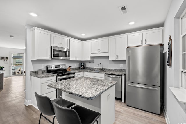 kitchen with light hardwood / wood-style floors, appliances with stainless steel finishes, light stone counters, and white cabinets