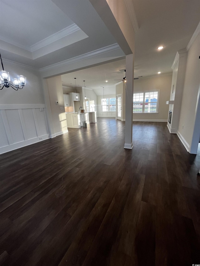 unfurnished living room with ceiling fan with notable chandelier, dark hardwood / wood-style flooring, and crown molding