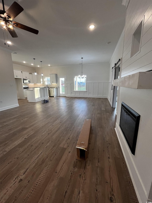 unfurnished living room featuring dark hardwood / wood-style floors, a barn door, crown molding, and ceiling fan with notable chandelier