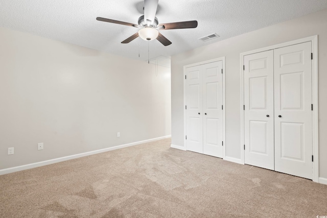 unfurnished bedroom with light carpet, a textured ceiling, two closets, and ceiling fan