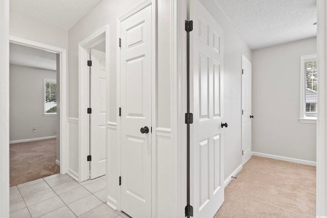 hall with a textured ceiling, light colored carpet, and a wealth of natural light