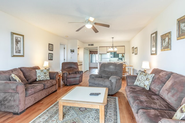 living room with ceiling fan with notable chandelier and light wood-type flooring