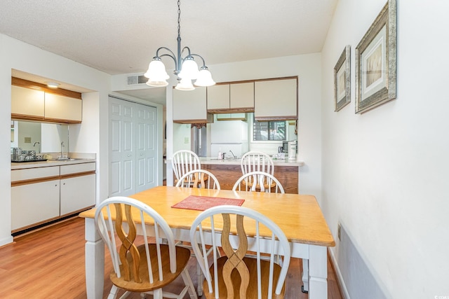 dining area with sink, a notable chandelier, light wood-type flooring, and a textured ceiling