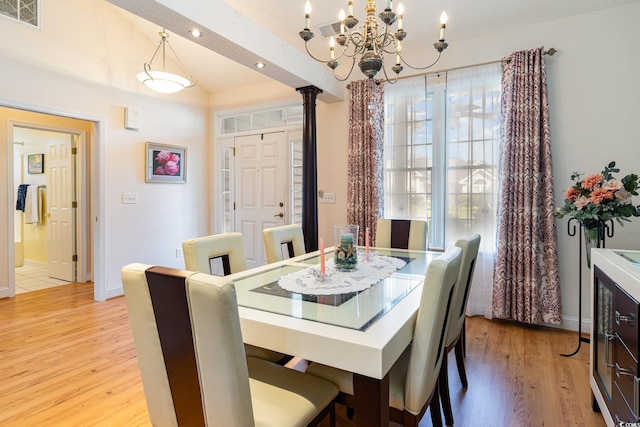 dining space with decorative columns, an inviting chandelier, and light hardwood / wood-style flooring