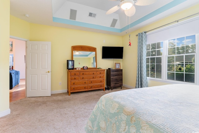 carpeted bedroom with a raised ceiling and ceiling fan