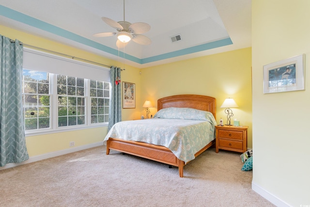 bedroom with a raised ceiling, ceiling fan, and light colored carpet