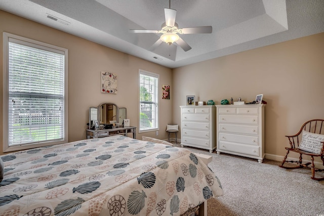 carpeted bedroom with a textured ceiling, a raised ceiling, and ceiling fan