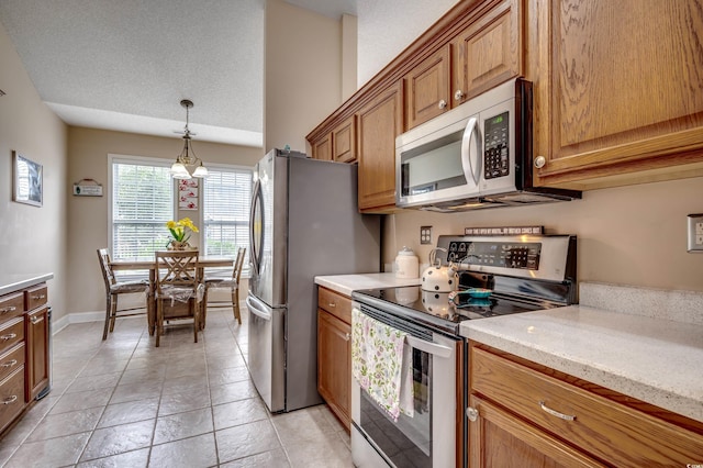 kitchen with light stone counters, a textured ceiling, appliances with stainless steel finishes, light tile patterned floors, and decorative light fixtures