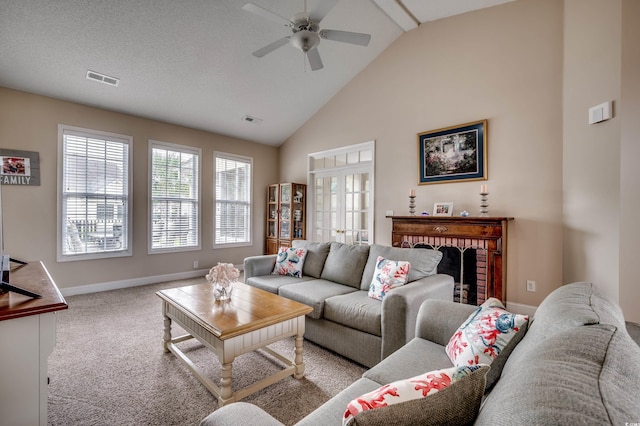 living room featuring high vaulted ceiling, a brick fireplace, a textured ceiling, ceiling fan, and light colored carpet