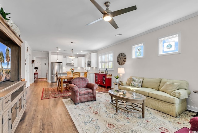 living room with light wood-type flooring, ornamental molding, and ceiling fan