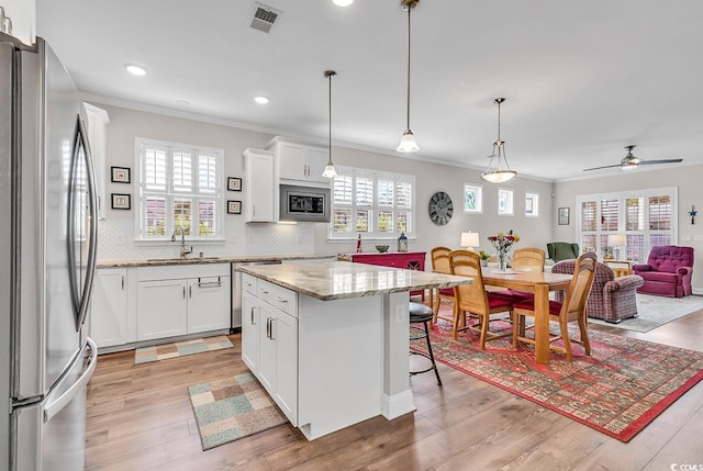 kitchen with light hardwood / wood-style floors, a center island, white cabinetry, stainless steel appliances, and decorative light fixtures