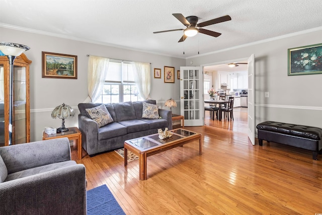 living room featuring light wood-type flooring, a textured ceiling, ornamental molding, and ceiling fan