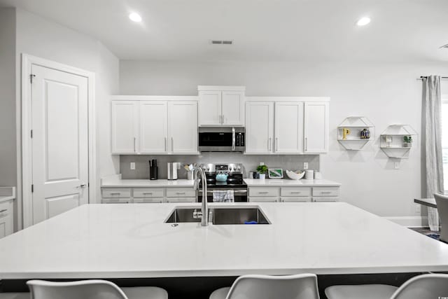 kitchen with stainless steel appliances, decorative backsplash, a breakfast bar, white cabinets, and a kitchen island with sink