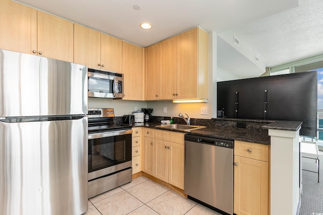 kitchen featuring light brown cabinets, sink, a textured ceiling, stainless steel appliances, and dark stone countertops