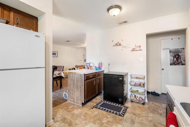 kitchen with dark brown cabinets, light wood-type flooring, white refrigerator, and fridge