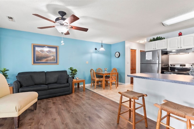 living room featuring light hardwood / wood-style flooring, ceiling fan, and a textured ceiling