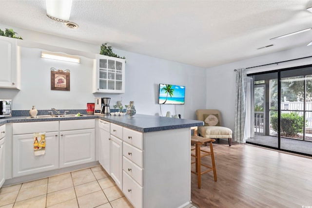 kitchen featuring a textured ceiling, sink, white cabinets, kitchen peninsula, and light hardwood / wood-style flooring