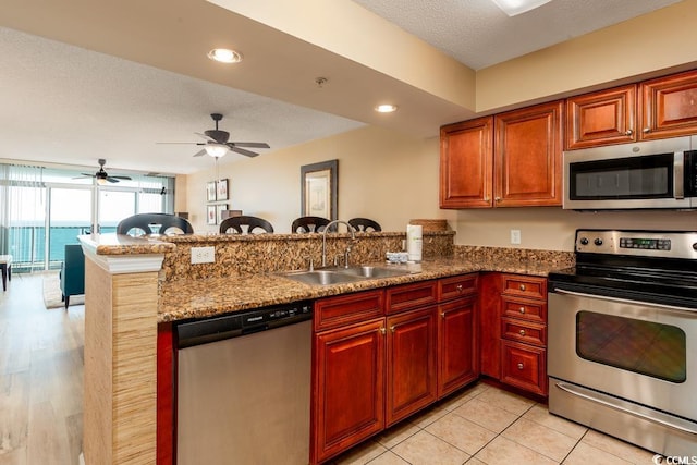 kitchen with a sink, a textured ceiling, recessed lighting, appliances with stainless steel finishes, and a peninsula