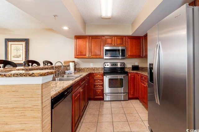 kitchen with light tile patterned floors, a peninsula, a sink, stainless steel appliances, and a textured ceiling