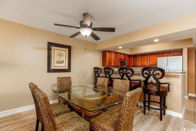 dining room with baseboards, a textured ceiling, a ceiling fan, and light wood finished floors