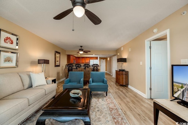 living area with a textured ceiling, light wood-style floors, baseboards, and ceiling fan