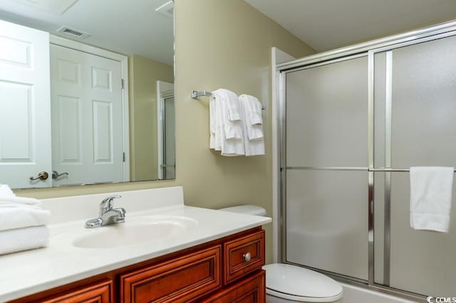 bathroom featuring vanity, toilet, visible vents, and a shower with shower door