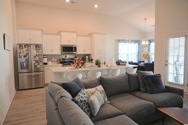 living room featuring high vaulted ceiling, light hardwood / wood-style flooring, and a chandelier