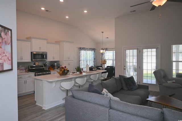 living room featuring ceiling fan, a healthy amount of sunlight, high vaulted ceiling, and light wood-type flooring