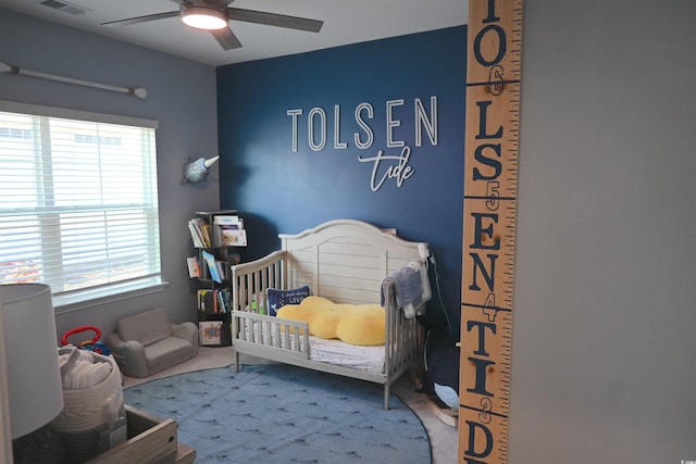 carpeted bedroom with ceiling fan and a crib