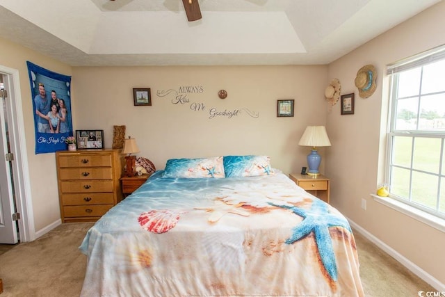 bedroom with a raised ceiling, ceiling fan, light colored carpet, and multiple windows